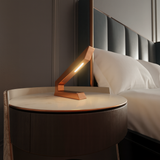 Copper finish handcrafted oak angular wooden lamp by WOOM, illuminating a marble bedside table next to a bed.