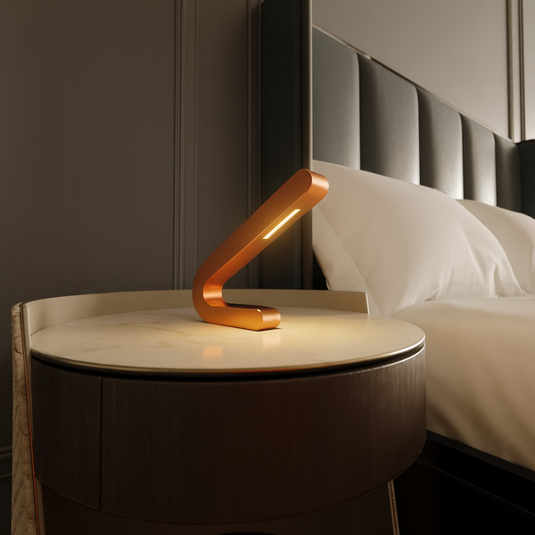 Angled copper finish table lamp by WOOM with a sleek bent design and illuminated LED strip, on a marble nightstand.