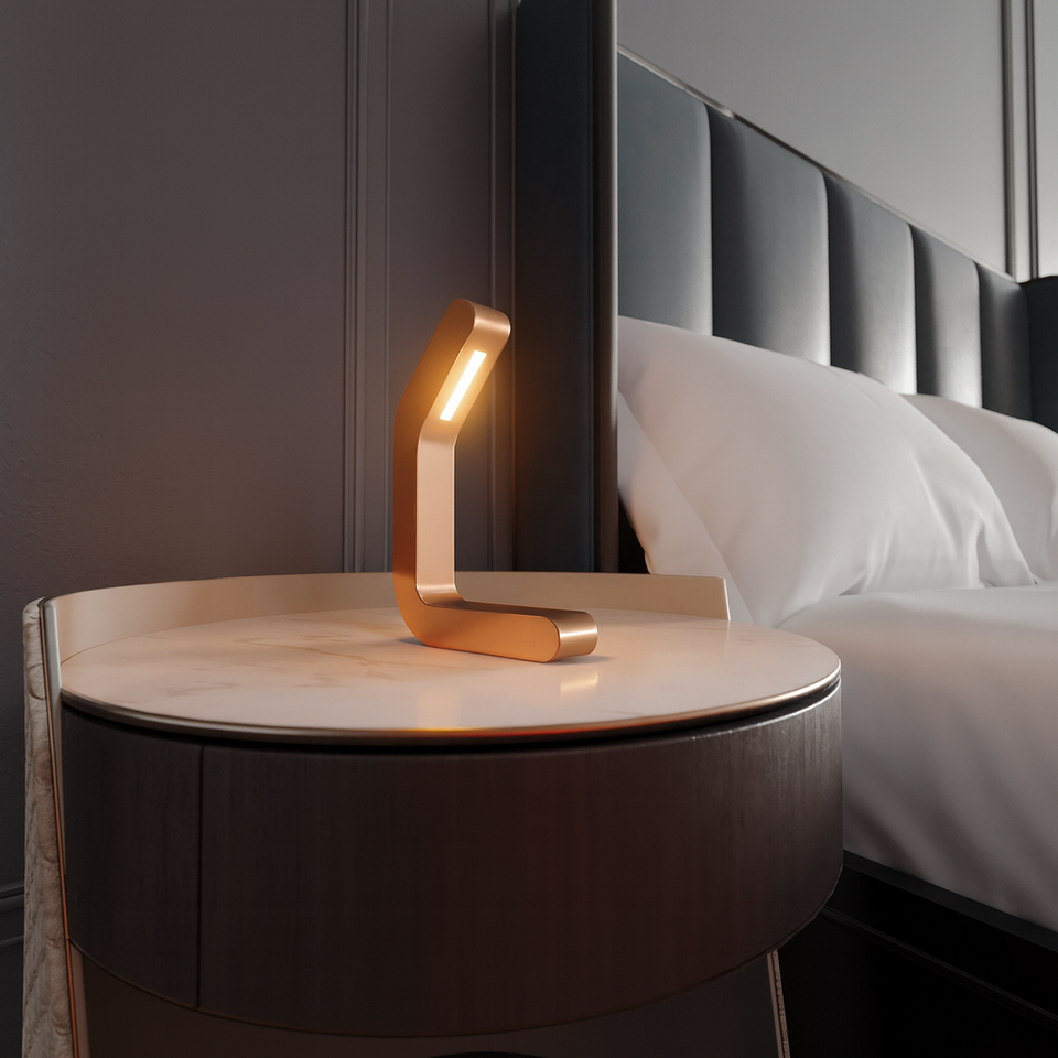 Curved copper-finish LED lamp by WOOM, resting on a white marble nightstand next to a bed.
