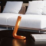 Copper finish L-shaped wooden lamp by WOOM with a bright light strip on a black marble table.