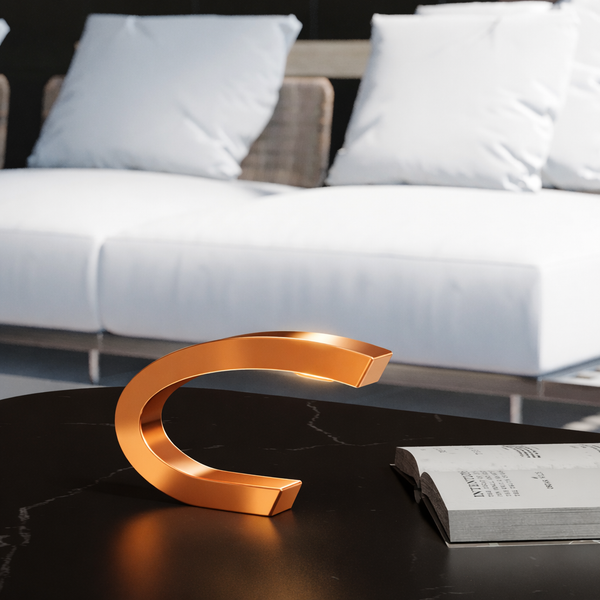 Copper finish Oak C-shaped curved wood lamp by WOOM, casting a soft glow on a black marble table.
