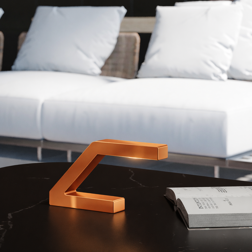 Z-shaped table lamp in copper finish by WOOM, featuring a minimalist design with a soft glow, on a dark marble table.