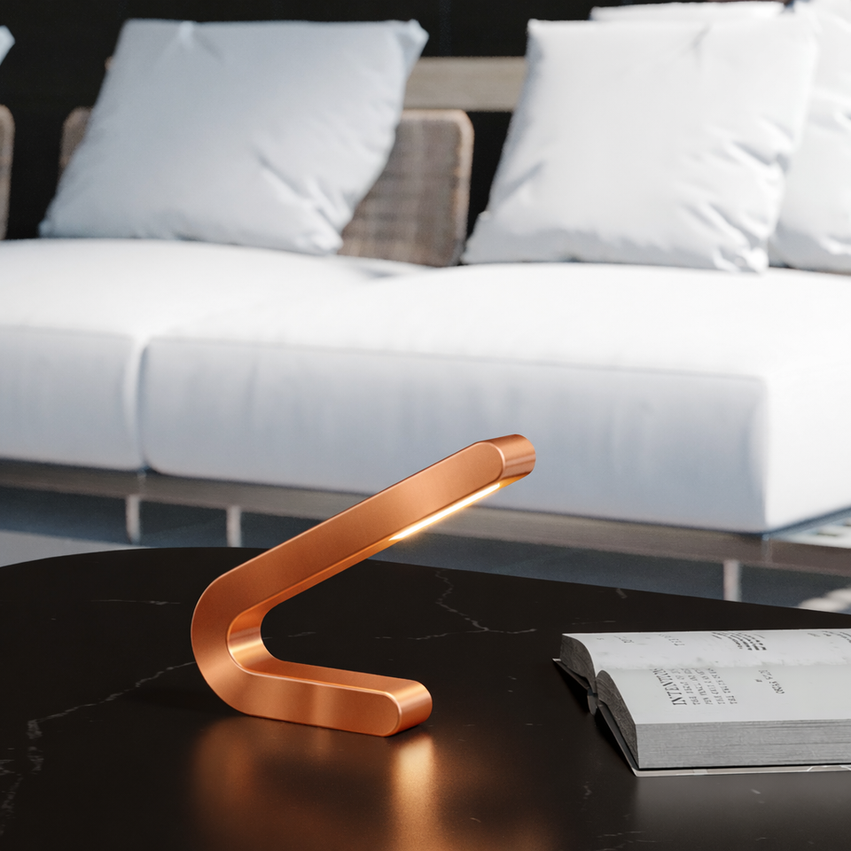 Angled copper finish table lamp by WOOM, casting a warm light on a dark marble table next to an open book.