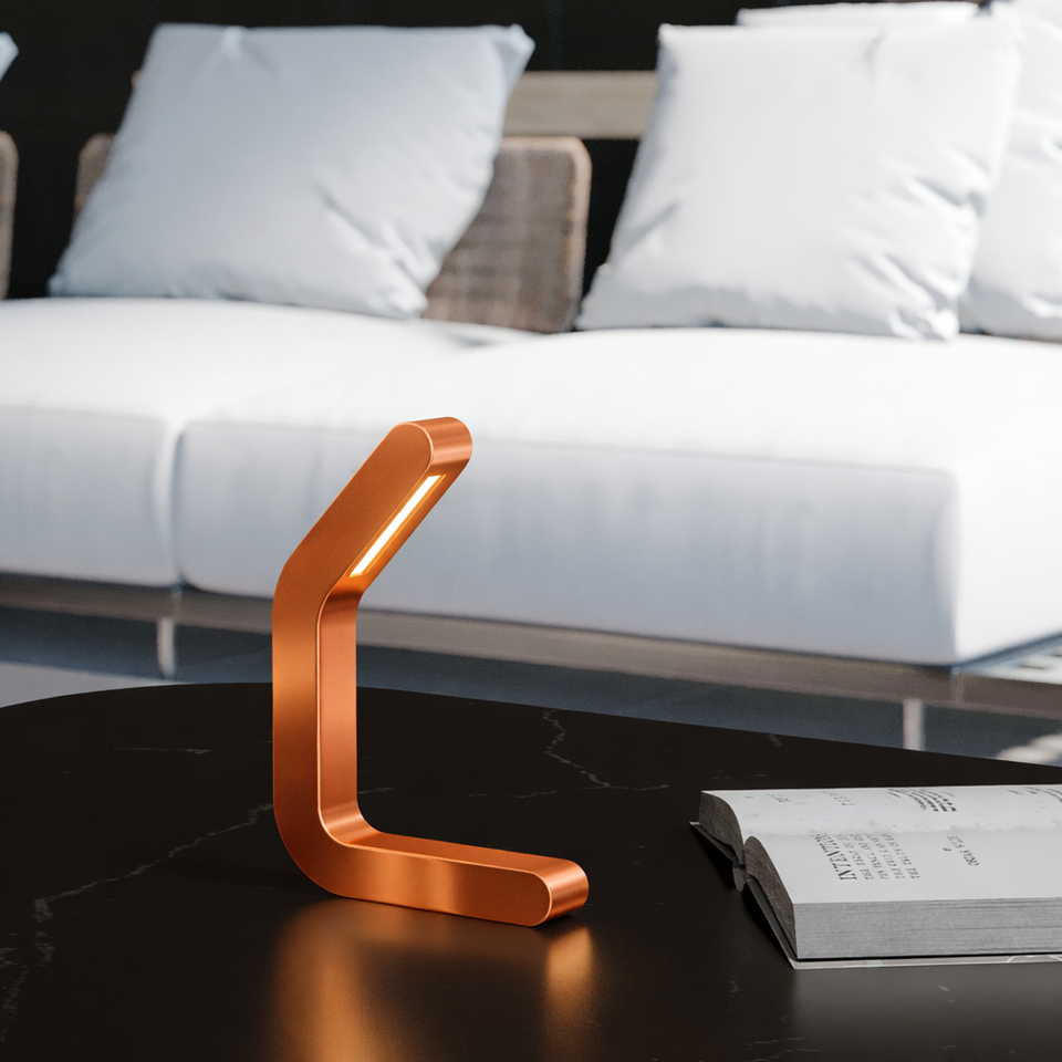 Curved wooden LED lamp with a copper finish by WOOM on a dark marble table beside an open book.