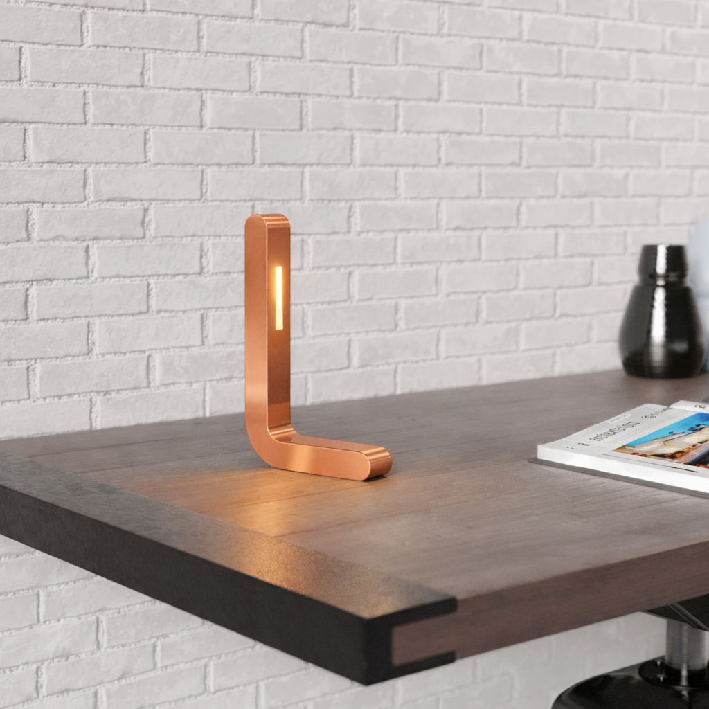 Copper finish oak L-shaped LED table lamp by WOOM, glowing on a dark wood desk.