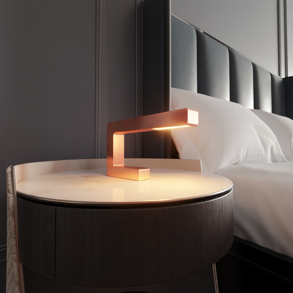 Copper finish C-shaped wooden table lamp by WOOM, emitting a warm glow on a marble-top nightstand.
