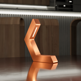 Copper geometric LED table lamp by WOOM with a bright light strip on a dark reflective surface.