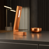 Handcrafted copper finish oak L-shaped LED lamp by WOOM, with a bright white light strip, on a dark gray surface.