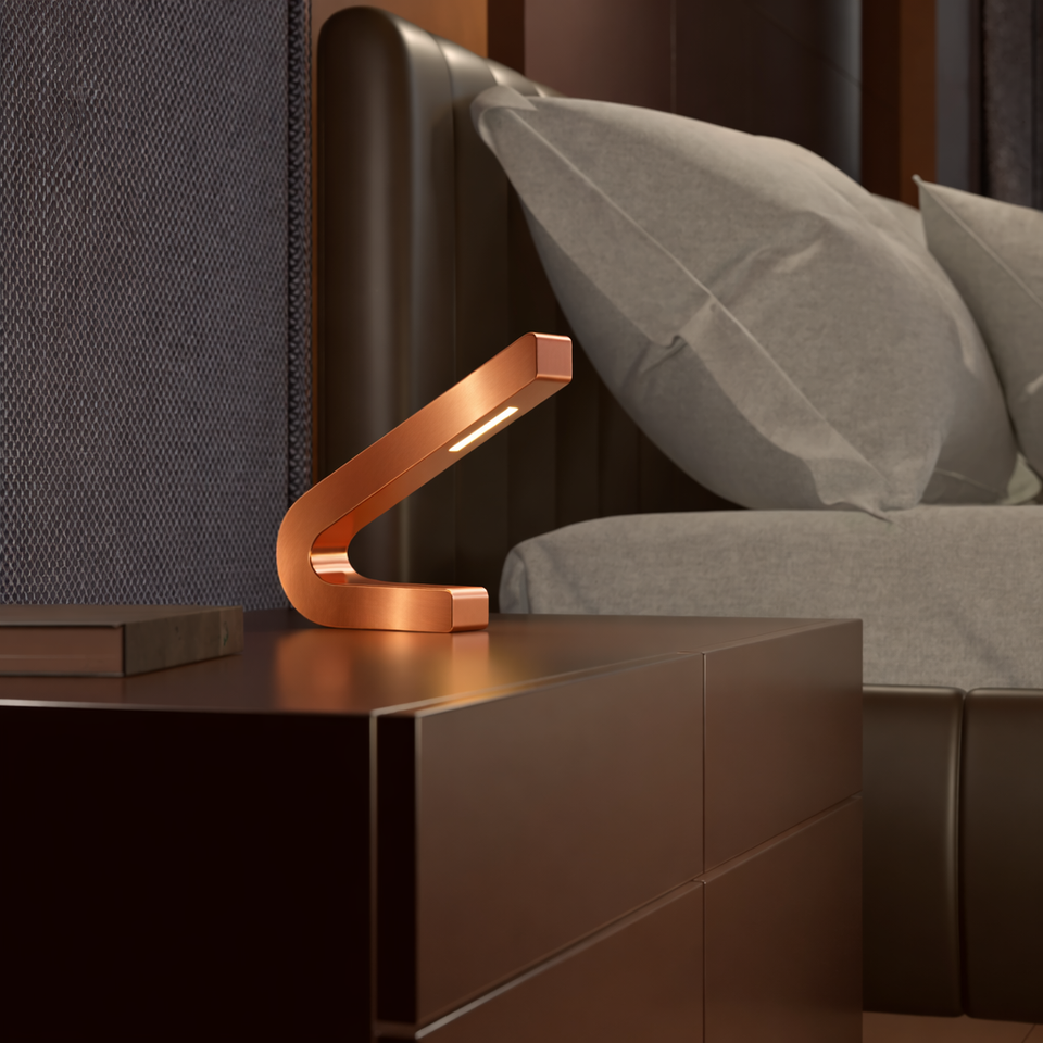 Handcrafted copper finish curved LED lamp by WOOM, glowing warmly on a dark bedside table.