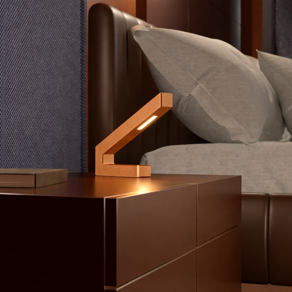 Copper finish oak LED lamp by WOOM with a modern V-shaped design emitting warm light on a dark nightstand.