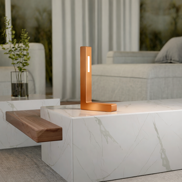 Copper-finished L-shaped contemporary oak table lamp by WOOM, featuring a vertical light strip on a marble coffee table.