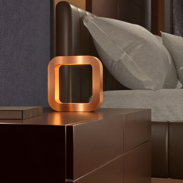 Copper finish square wooden lamp by WOOM on a dark brown nightstand with a book.