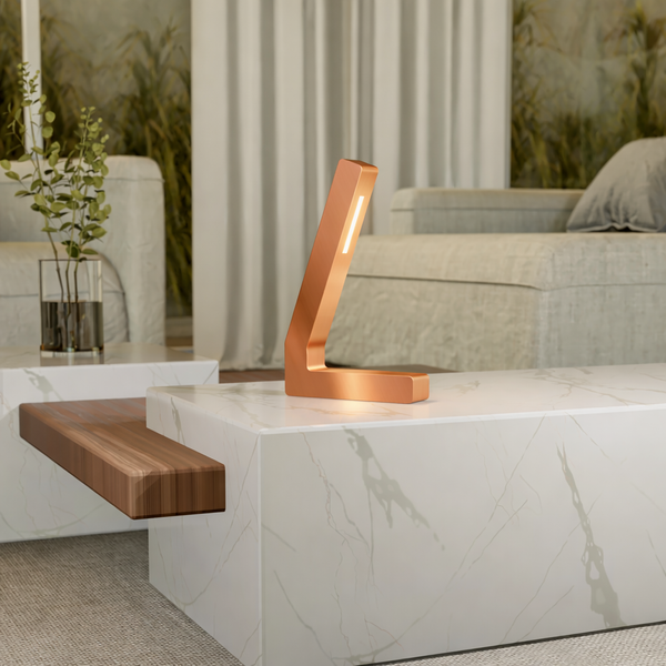Copper finish L-shaped LED lamp by WOOM with a glowing strip, on a white marble table.
