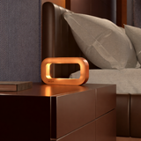 Copper finish rectangular lamp by WOOM emitting a warm glow, on a dark nightstand.