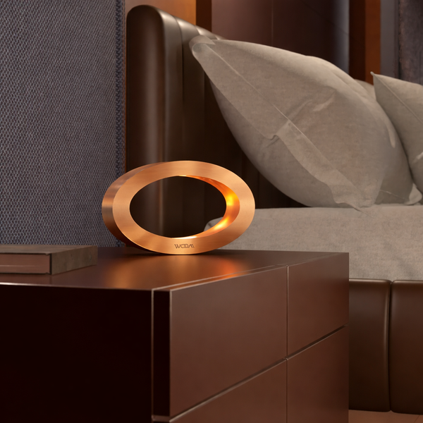 Rotatable copper finish wooden oval lamp by WOOM, glowing warmly on a dark nightstand in a modern bedroom.