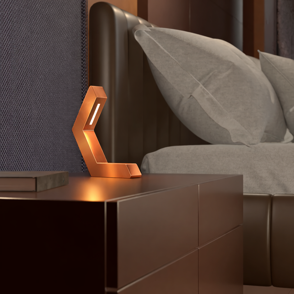 Copper finish geometric LED lamp by WOOM on a dark nightstand next to a bed.