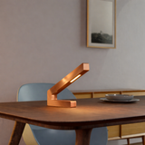 Handcrafted copper finish oak modern design LED lamp by WOOM, an L-shaped light on a wooden table.