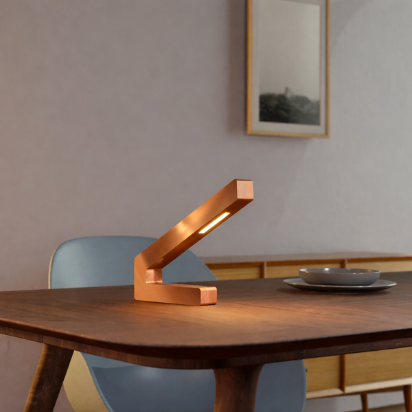 Handcrafted copper finish oak modern design LED lamp by WOOM, an L-shaped light on a wooden table.