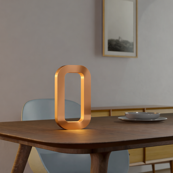 Copper finish rotatable rectangular lamp by WOOM, handcrafted from oak wood and glowing warmly on a dark table.