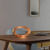 Copper Finish Handcrafted Rotatable Wooden Oval Lamp by WOOM, casting a warm glow on a wooden table.