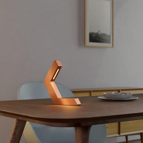 Copper finish geometric LED lamp by WOOM, radiating a warm glow on a wooden dining table.
