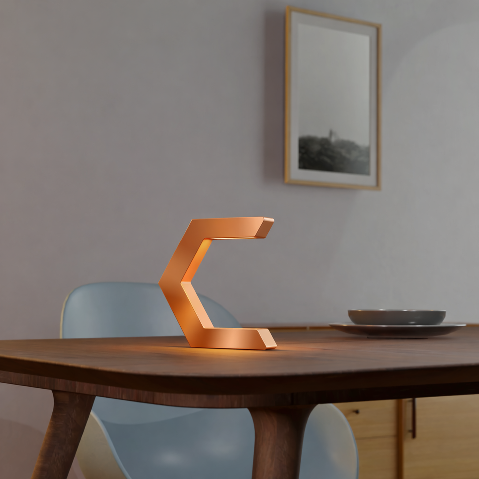 Copper finish C-shaped lamp by WOOM, emitting a warm glow, displayed on a dark wooden table.