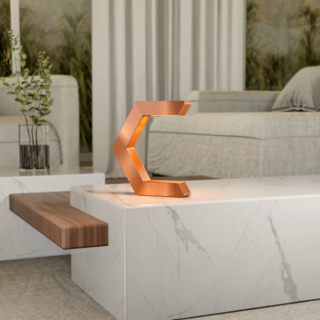 Copper finish C-shaped lamp by WOOM with an illuminated interior, placed on a white marble table.
