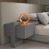 Handcrafted copper finish oak rotatable hexagon table lamp by WOOM, glowing softly on a grey floating bedside table beside a textured bed.
