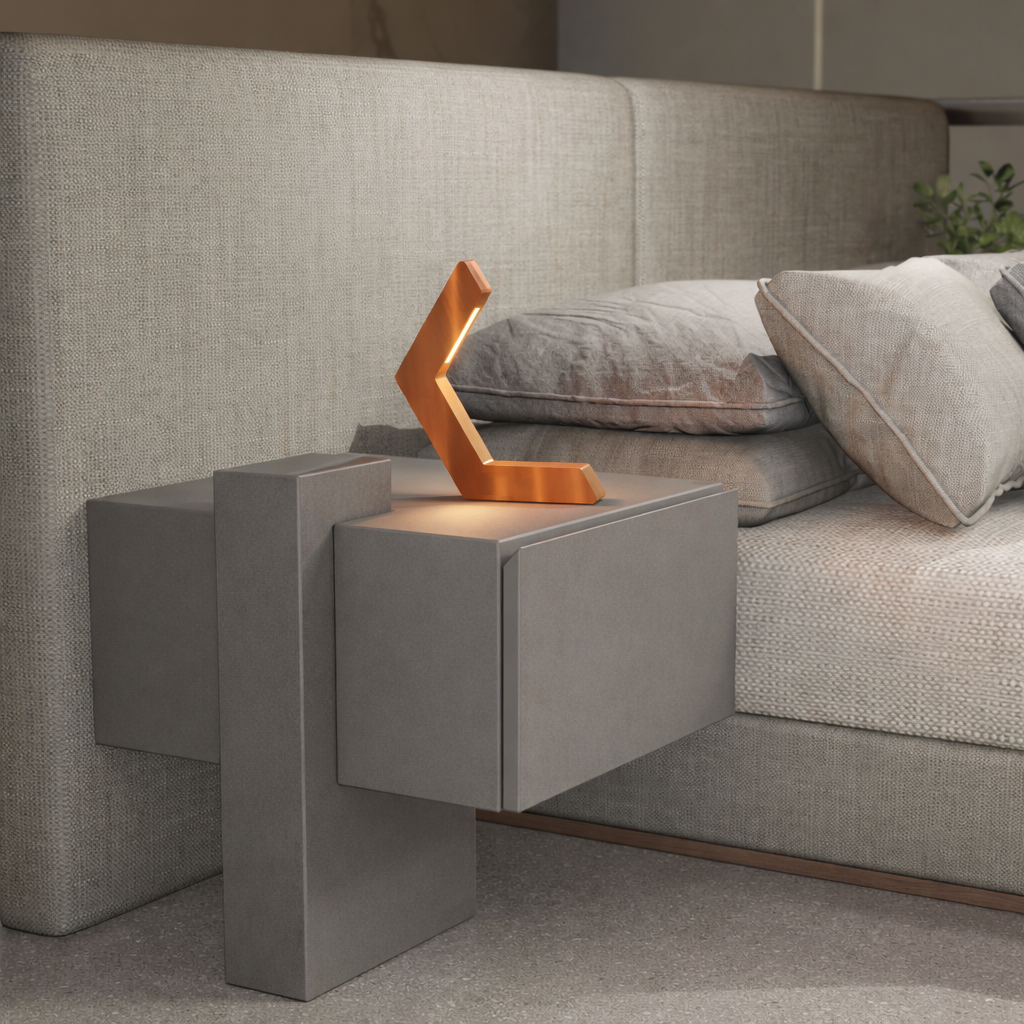 Copper finish geometric LED table lamp by WOOM, with a V-shaped design, sits on a grey nightstand.