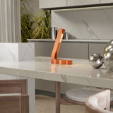 Handcrafted copper finish oak L-shaped LED lamp by WOOM on a white marble countertop with decorative chrome balls.
