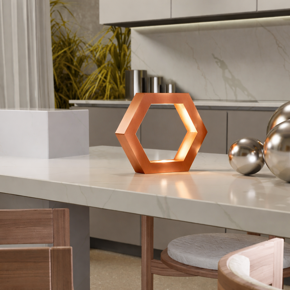 Handcrafted copper finish hexagon lamp by WOOM, glowing brightly on a white kitchen island next to silver spheres.