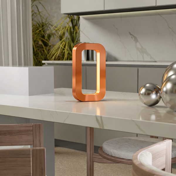 Copper finish rectangular oak table lamp by WOOM, glowing softly on a marble kitchen island with silver spheres.