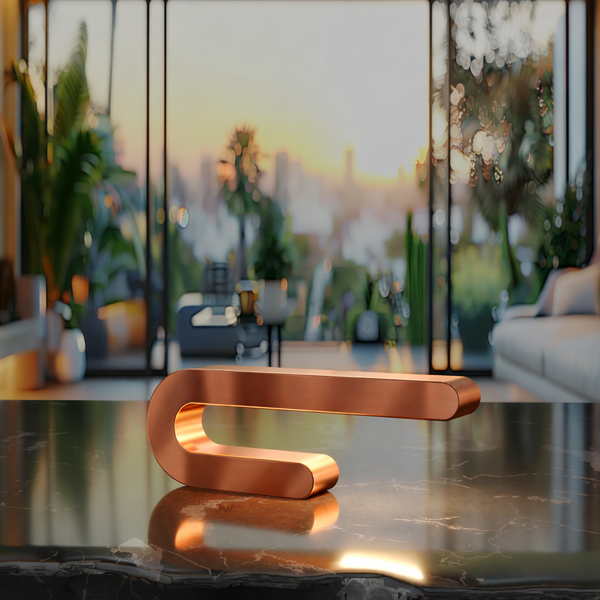 Copper finish U-shape curved lamp by WOOM, on a dark marble table with a blurred modern interior background.