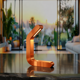Curved copper finish LED lamp by WOOM, illuminated on a dark marble countertop in a modern living room with a sunset city view.