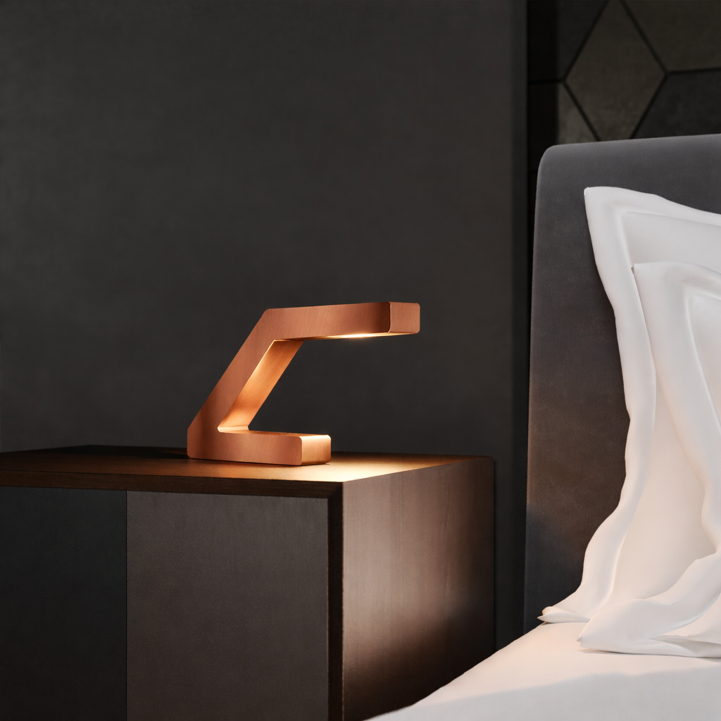 Copper finish Z-shaped lamp handcrafted from oak by WOOM, illuminating a dark nightstand in a bedroom setting.