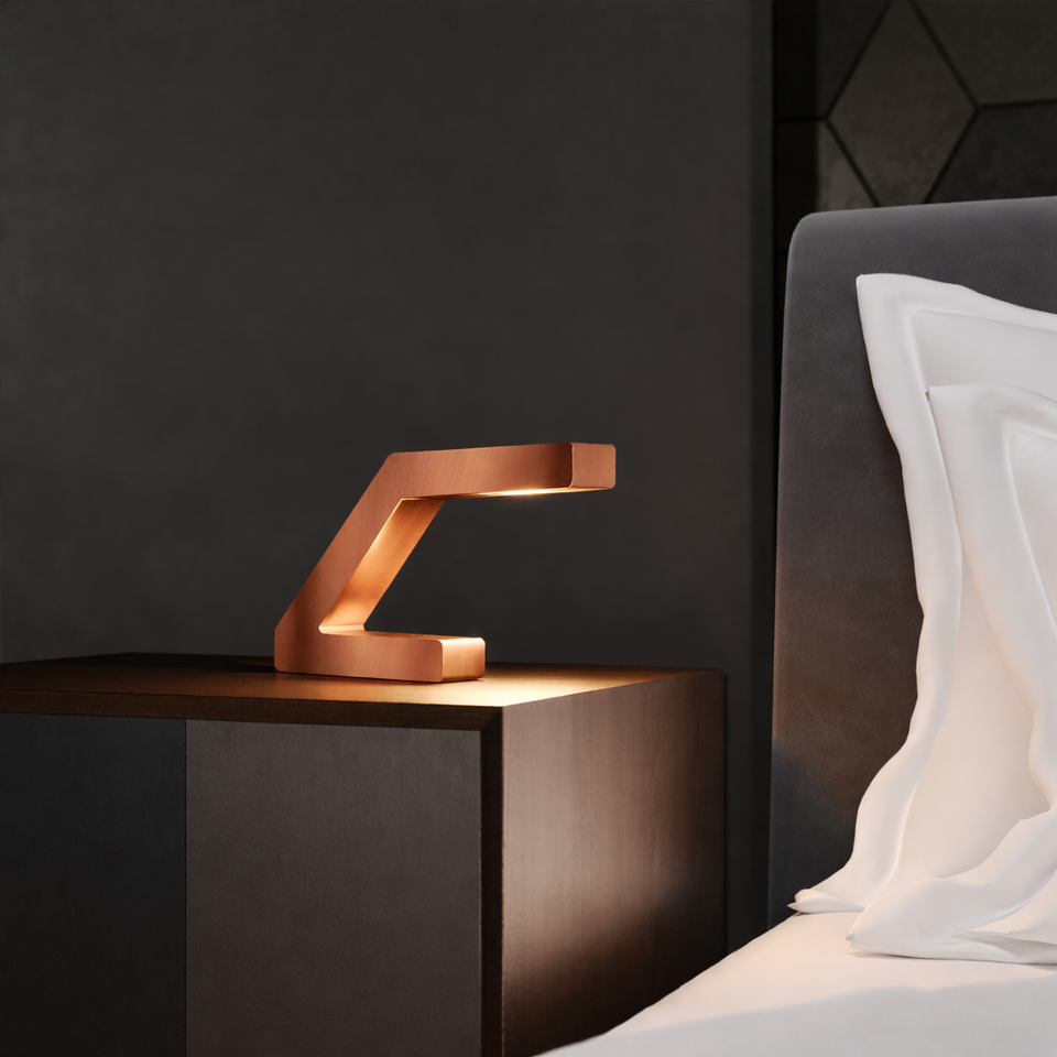 Copper finish Z-shaped lamp handcrafted from oak by WOOM, illuminating a dark nightstand in a bedroom setting.