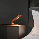 Copper finish angled wooden table lamp by WOOM, with a sleek bent-arm design glowing softly.
