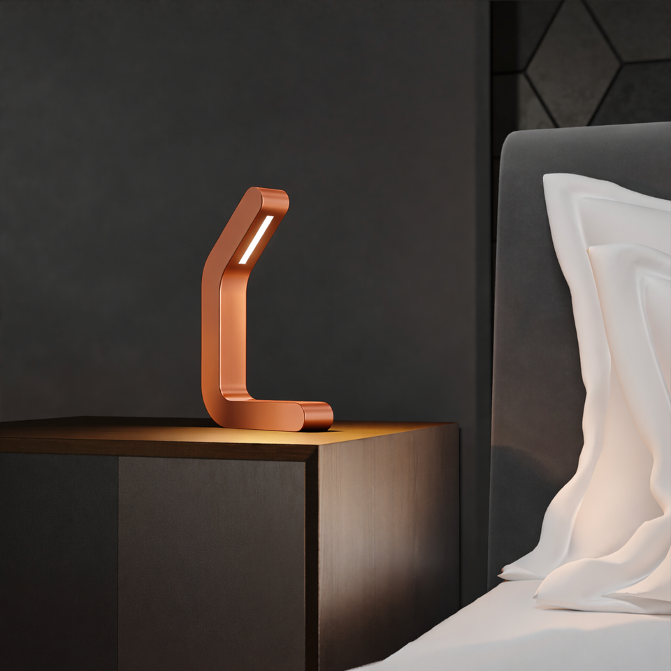 Copper finish oak curved LED lamp by WOOM, illuminating a dark wood bedside table next to a bed.