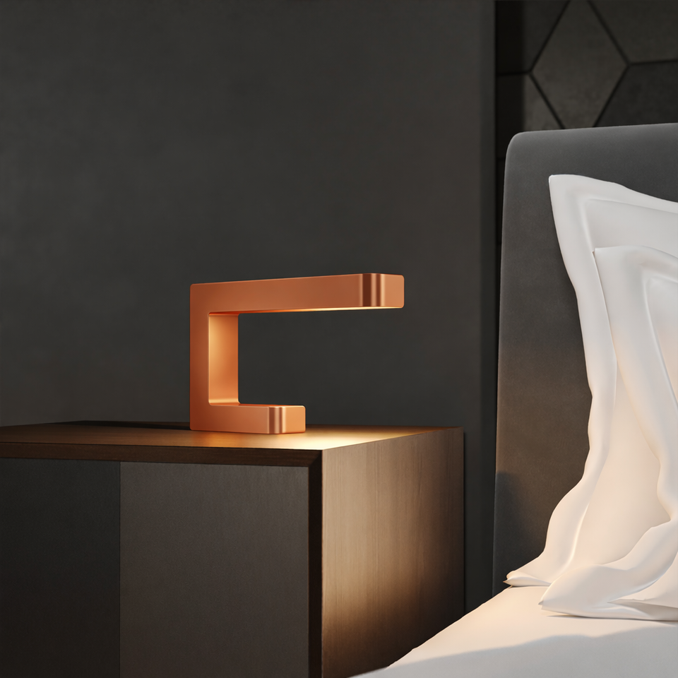 Copper finish wooden C-shaped lamp by WOOM on a dark nightstand, emitting a warm glow.