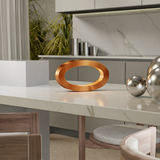 Smooth, reflective copper oval loop lamp by WOOM on a white marble kitchen counter.
