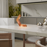 Copper finish geometric LED lamp by WOOM on a white marble counter, emitting a warm glow, with silver spheres nearby.