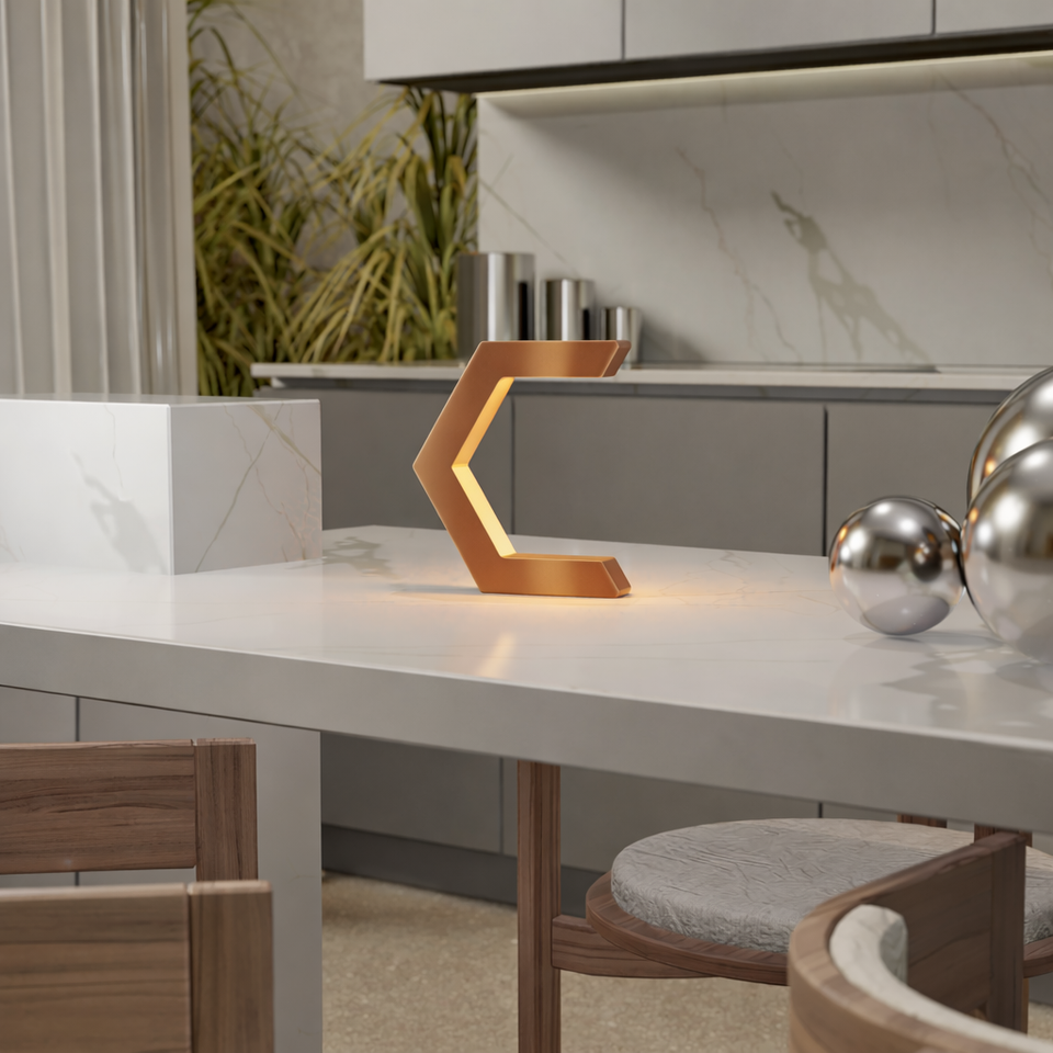 Copper finish C-shaped table lamp by WOOM, glowing on a white marble countertop with chrome spheres.