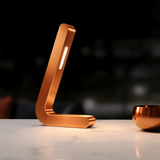 Copper-finish L-shaped oak lamp by WOOM, with an illuminated LED strip, on a white marble table.