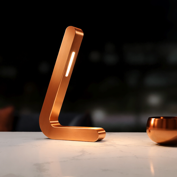 Copper-finish L-shaped oak lamp by WOOM, with an illuminated LED strip, on a white marble table.