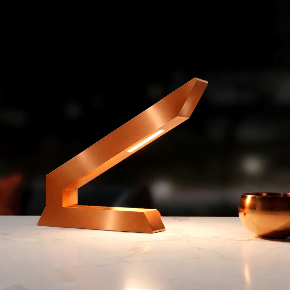 Copper-finished angular oak wooden lamp by WOOM, with an integrated LED strip, displayed on a white marble table next to a copper bowl.