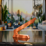 Angular copper finish table lamp by WOOM, with a brushed texture, emitting a warm glow on a dark marble counter.