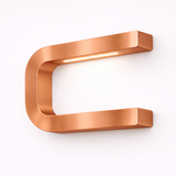 Copper finish U-shape curved lamp by WOOM with an integrated LED light strip, featuring a brushed texture on a white wall.