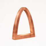 Copper finish curved arch desk lamp by WOOM, with a brushed texture and subtle internal glow.