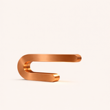 Copper U-Shape Curved Lamp by WOOM, with a smooth brushed metallic finish on a light background.