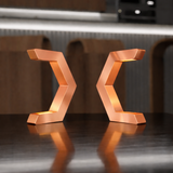 Two copper finish C-shaped table lamps by WOOM, arranged symmetrically forming an X, with warm internal light.